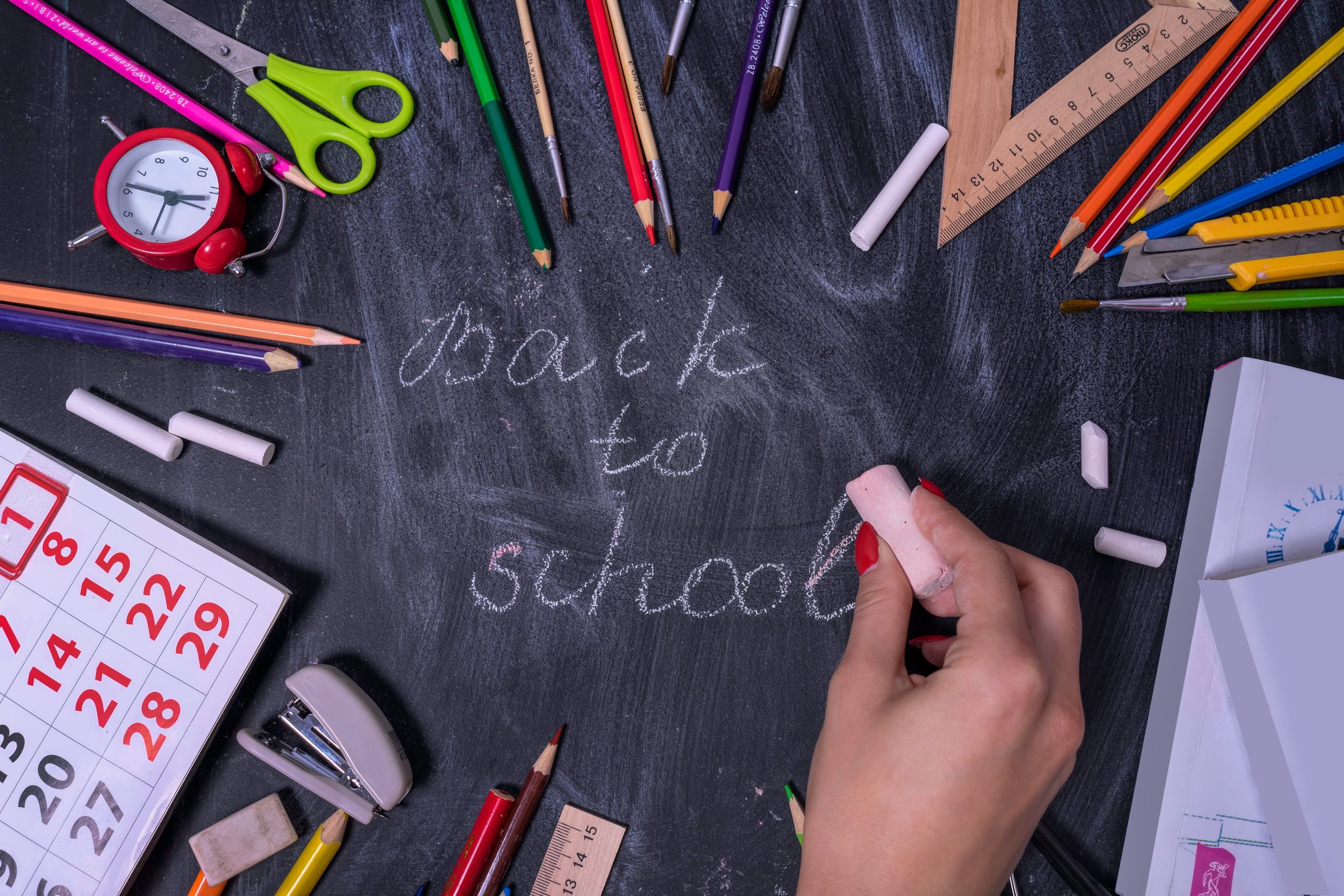Fournitures de rentrée scolaire et calendrier autour d'un tableau noir où est écrit « back to school »